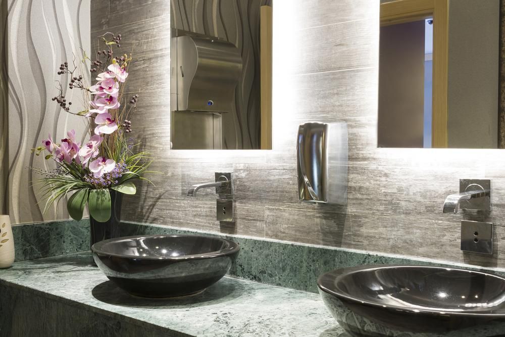 Bathroom with two black bowl sinks on a green countertop, mirrors, and a flower arrangement.