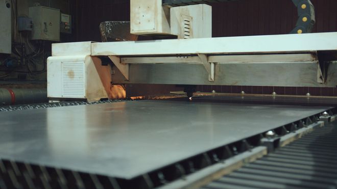 Metal sheet being cut by a laser cutter machine in a factory.