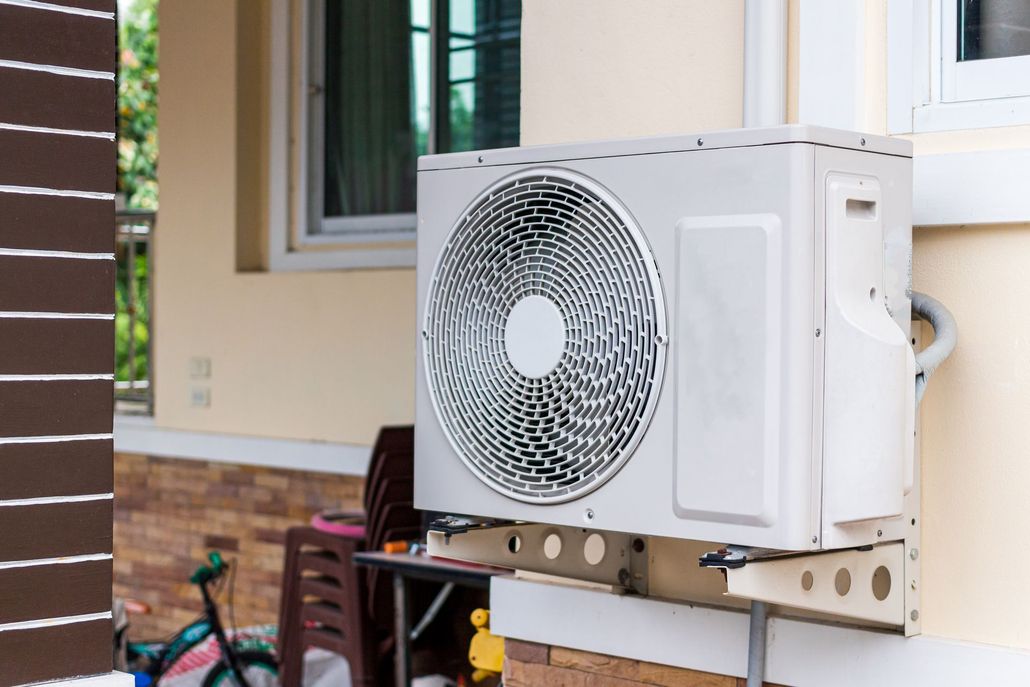 Air conditioning unit mounted on a light-colored building exterior, near a window.