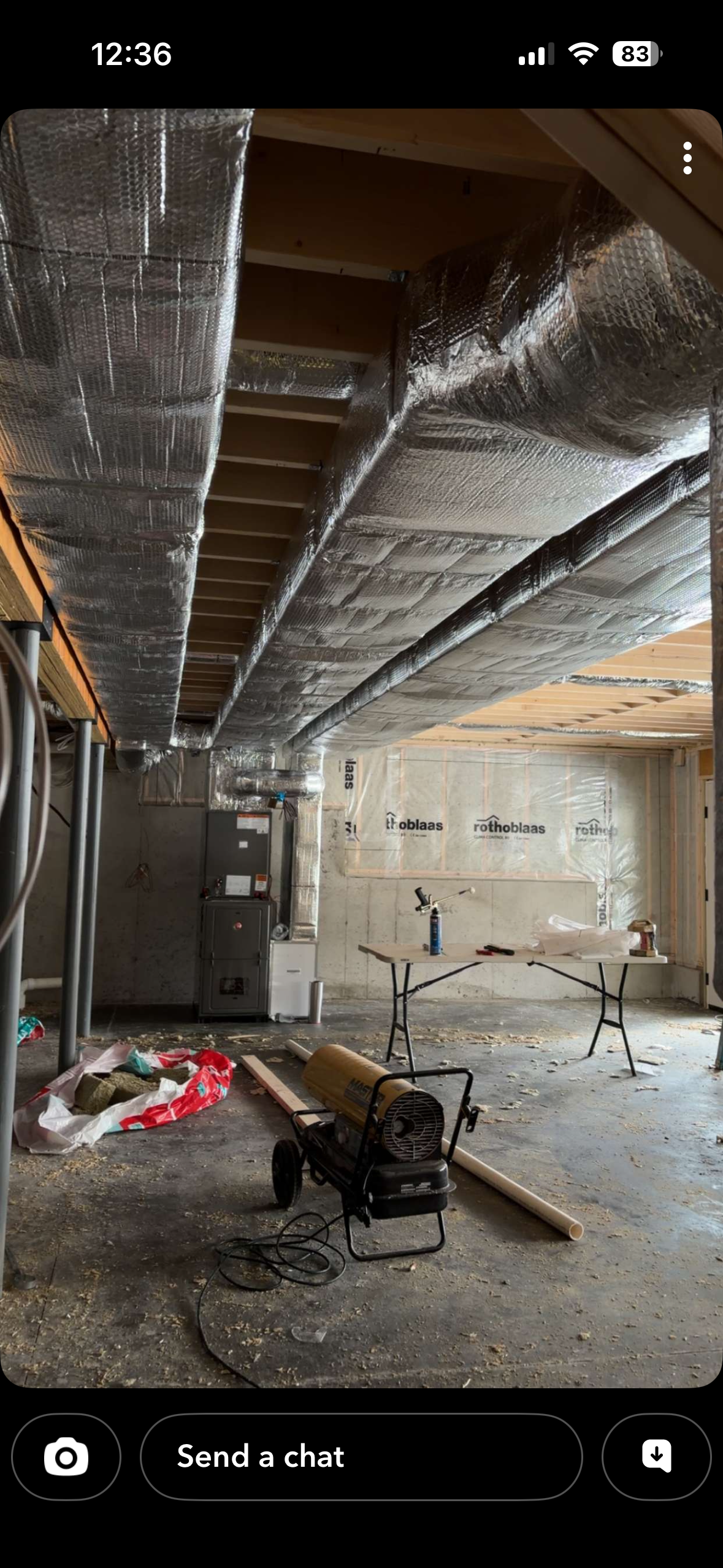 Interior view of a construction site with metallic insulation on the ceiling and tools and debris on the floor.