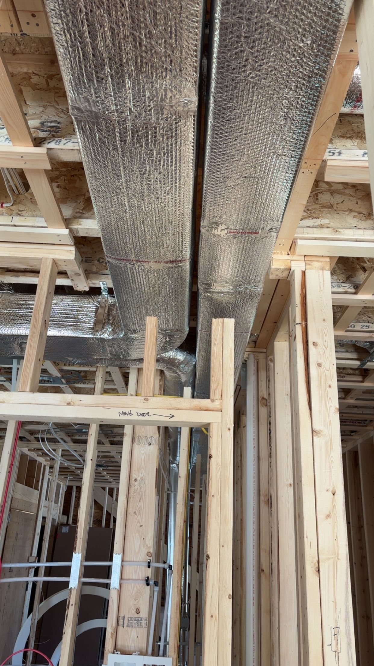 Ceiling with exposed pipes, ducts, and lighting in an office setting.