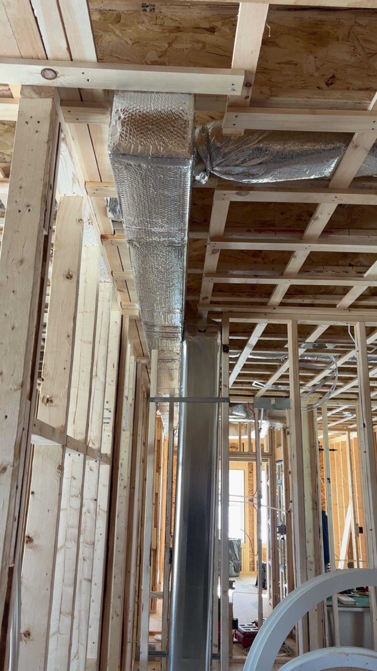 Framing of a house with exposed wood, a vertical metal duct, and unfinished ceilings.