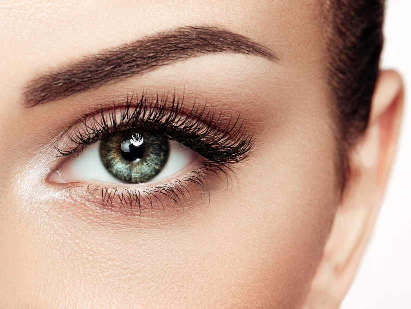 A close up of a woman 's green eye with long eyelashes.