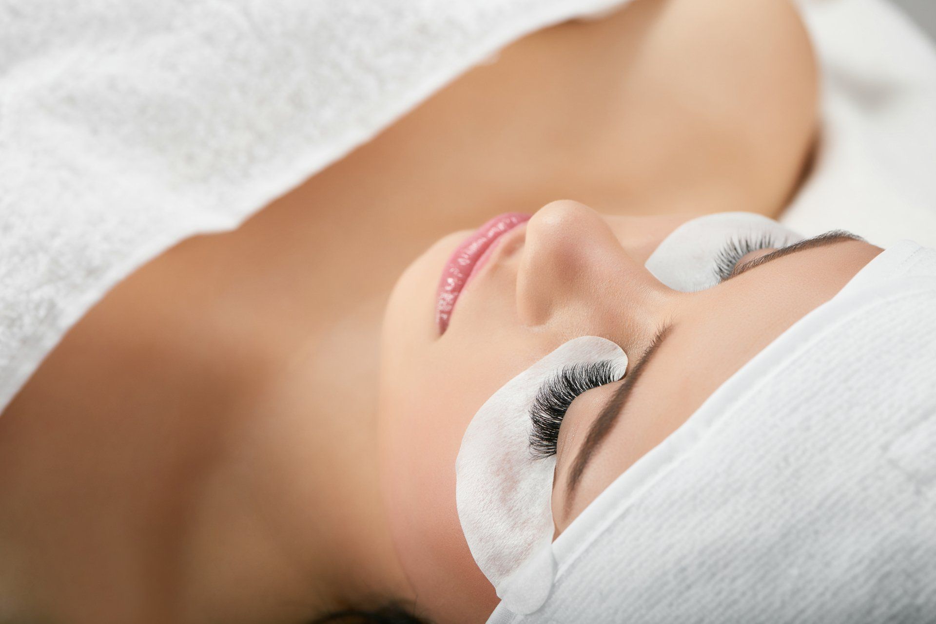 A woman is laying on a bed with a towel on her head and a bandage on her eyes.