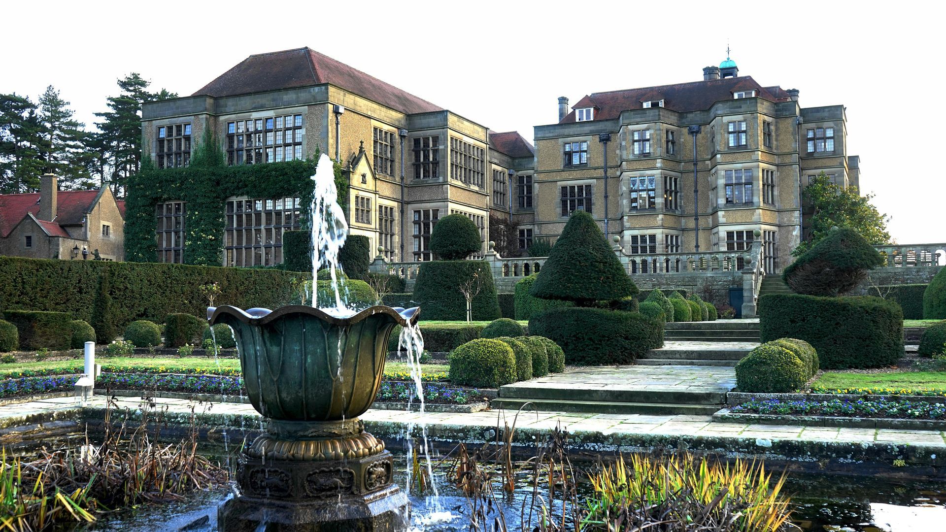 Formal gardens with fountains, trimmed hedges, and a large stone mansion.