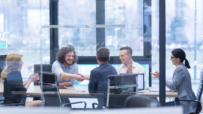 Reunião de negócios: pessoas apertando as mãos, sorrindo, batendo palmas em um escritório moderno.