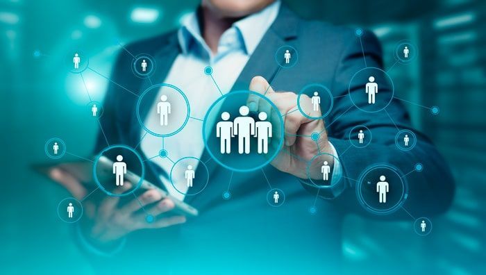 Empresário tocando uma tela digital com figuras humanas interconectadas, representando networking ou gerenciamento de equipe.