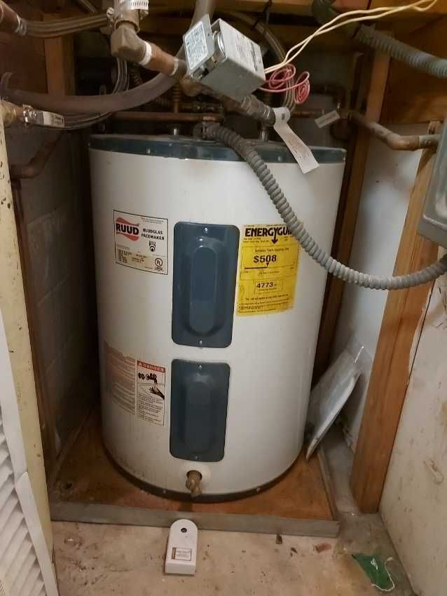 A white water heater is sitting in a corner of a room.