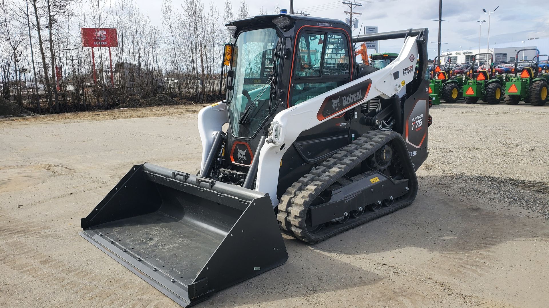 Bobcat T76 Skidsteer with bucket and forks Bobcat T76 compact track loader with black bucket in a gravel lot.