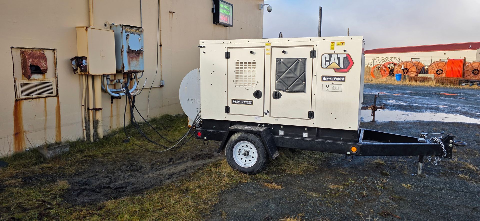 CAT XQ35 35 KWA portable generator Generator on a trailer parked next to a building. The building is beige with rusted electrical boxes.
