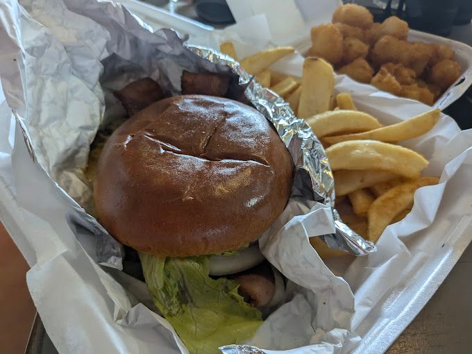 Hamburger, fries, and tater tots in takeout containers, wrapped in foil.