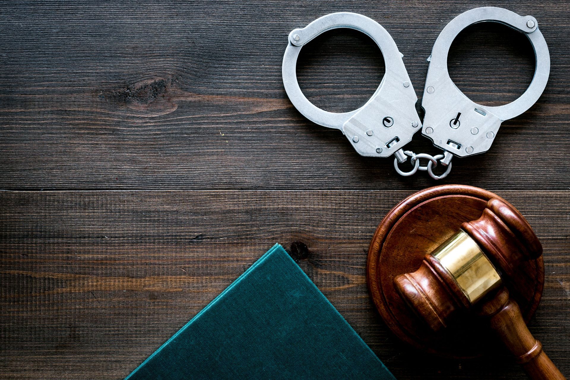 A pair of handcuffs and a judge 's gavel on a wooden table.