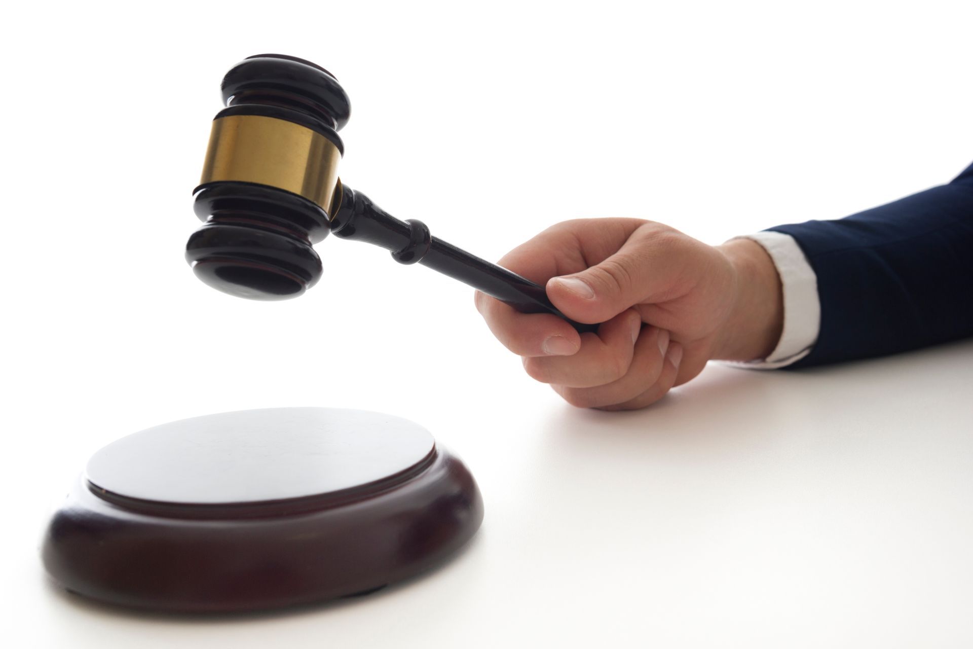 Hand holding a gavel, striking a wooden block on a white surface.