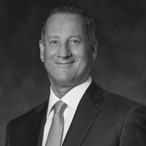 Man in a suit smiles, tie, and a dark background.