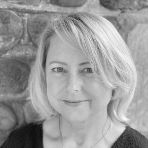 Woman with blonde hair, smiling, in front of a stone wall.