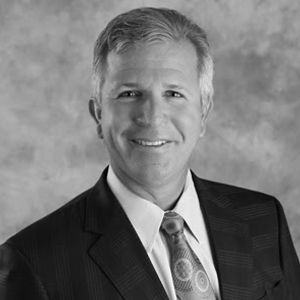 Man in suit smiling, looking at the viewer. Black and white, formal portrait.