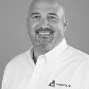 Man in white collared shirt with bald head and goatee, smiling.