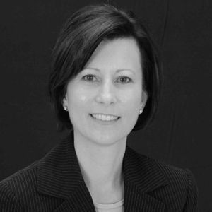 Woman with short dark hair in a suit jacket smiles at the camera.