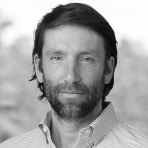 Man with a beard, in a button-down shirt, looking directly at the camera. Black and white.