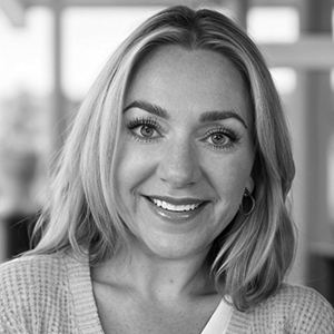 Woman with blonde hair smiling in a close-up, indoors.