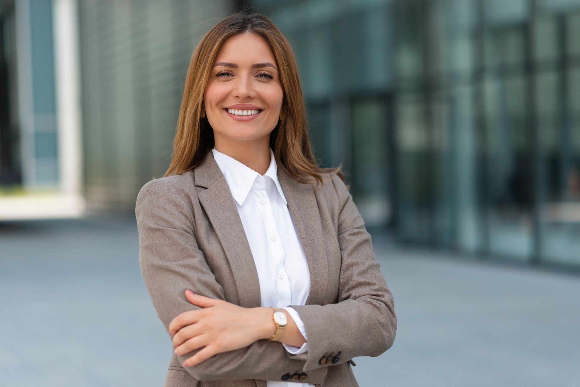Woman in business attire with arms crossed, smiling, standing outdoors.
