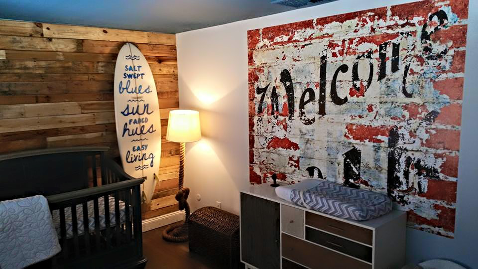 A room with a crib , dresser , lamp and a welcome sign on the wall.