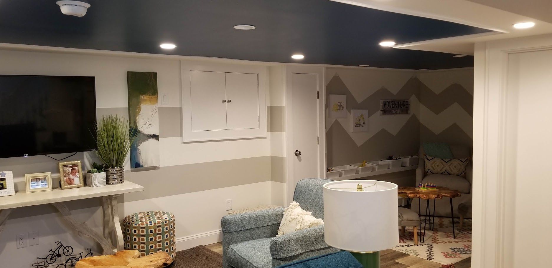 Living room with blue ceiling, white and gray walls. Includes a tv, couch, lamp, and art.