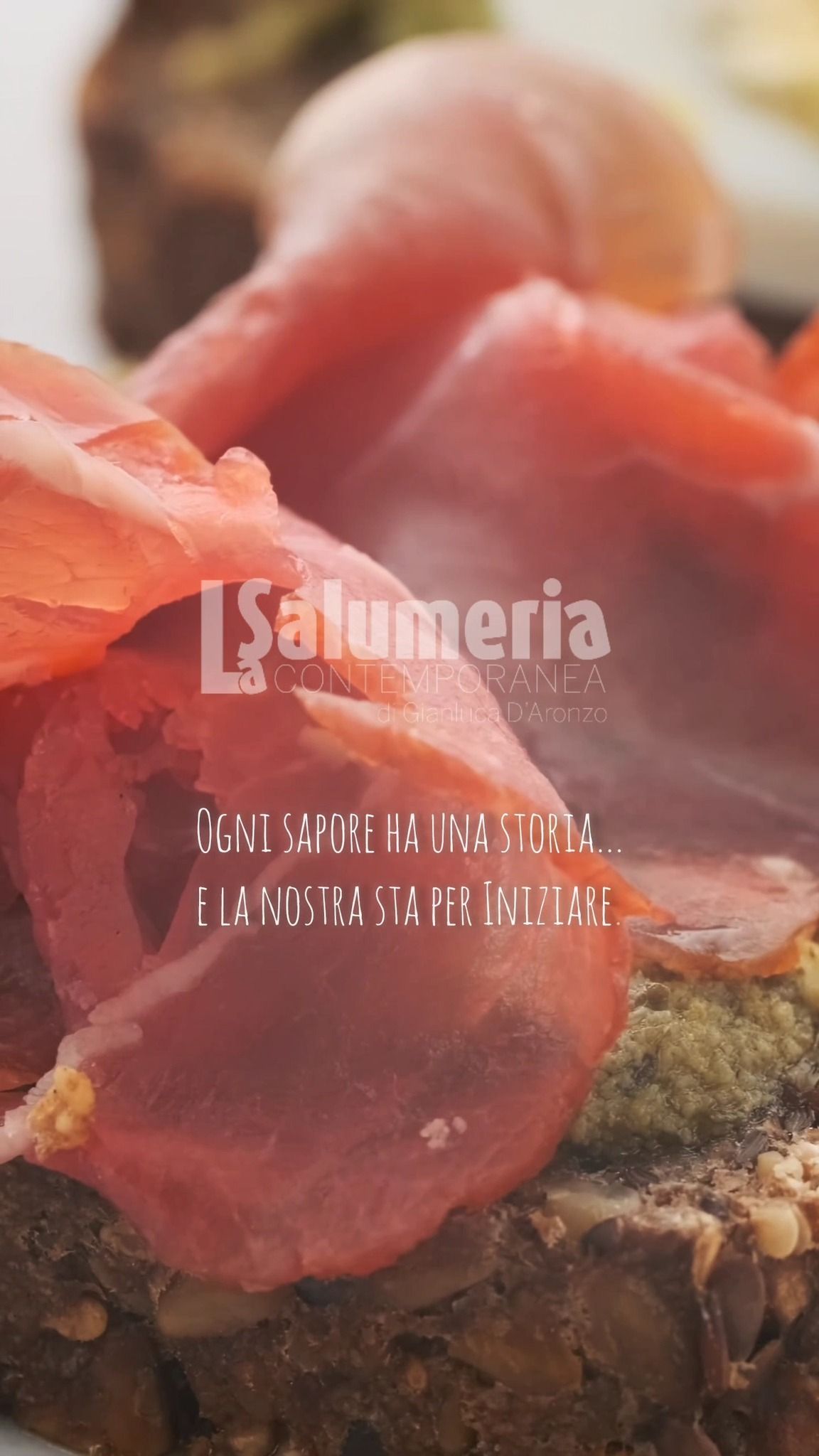 Primo piano di una fetta di pane condita con affettati di carne stagionata, probabilmente coppa.