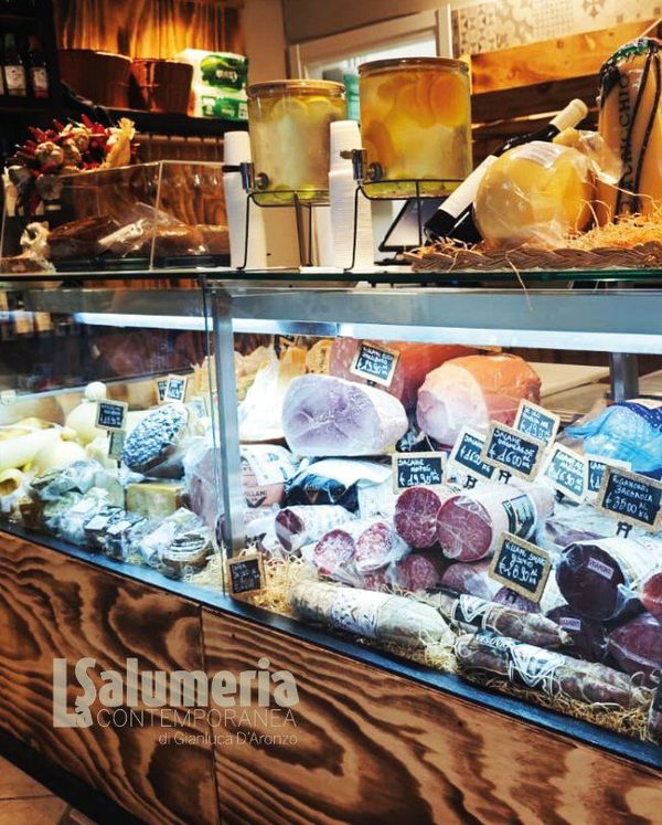 Vetrina piena di formaggi e salumi in un negozio.