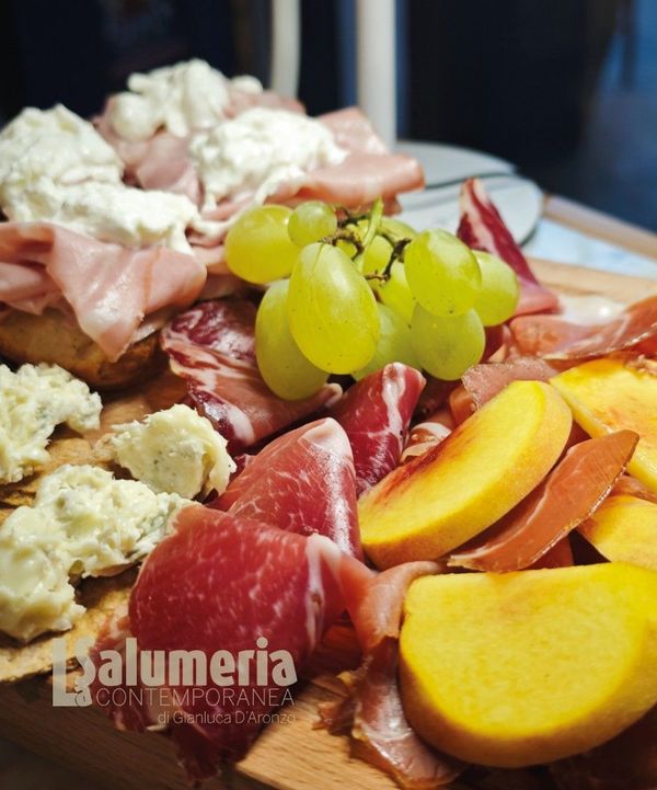 Tagliere di salumi con uva, prosciutto, pesche, formaggio e salame.