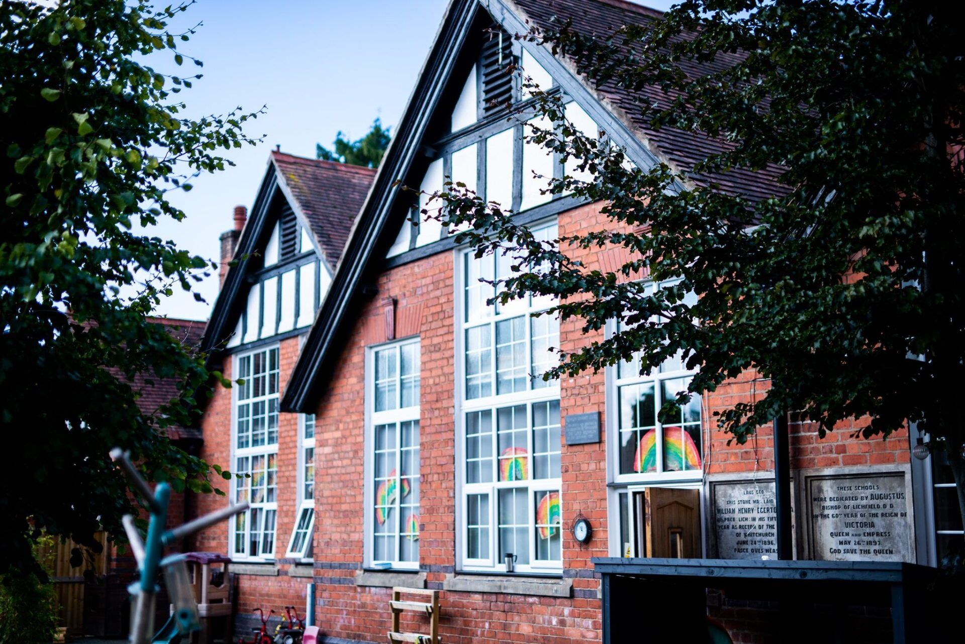 Red brick school building with white trim, windows, and a peaked roof with timber framing; surrounded by trees.