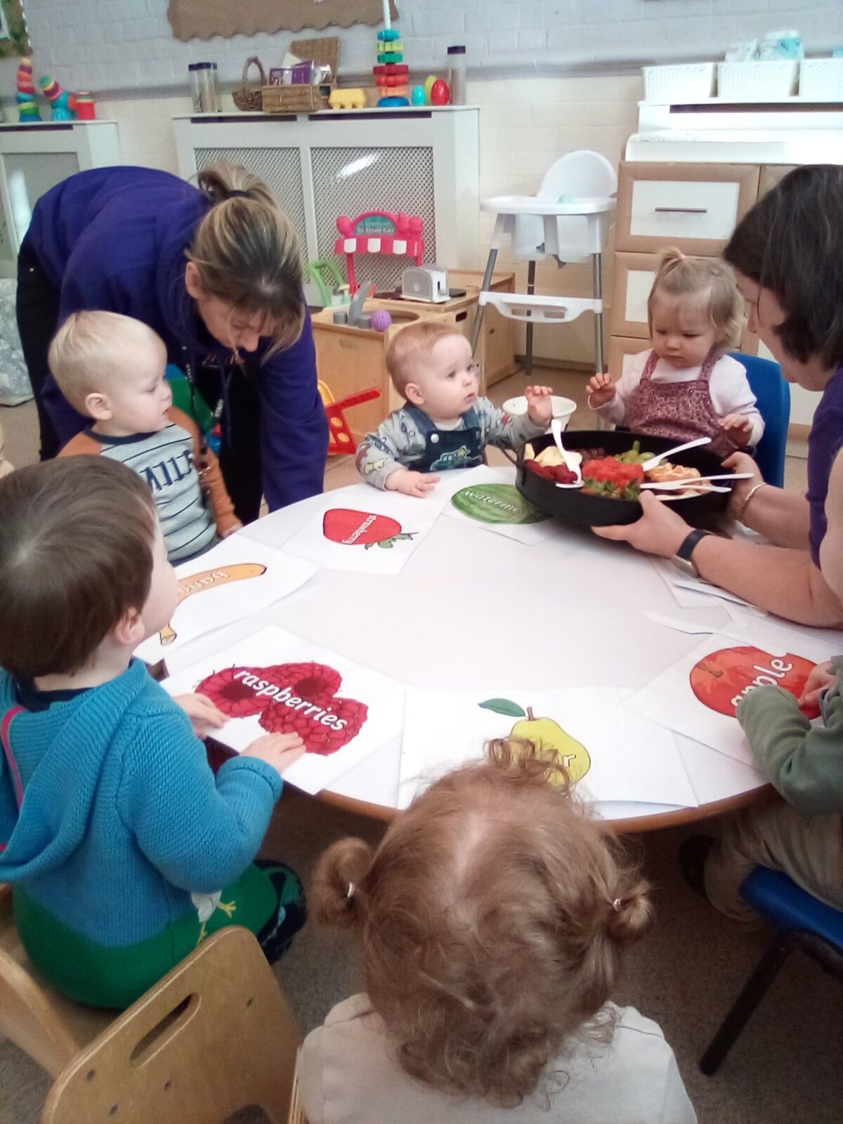 Children and adults at a table with fruit, focused on a fruit-themed activity.