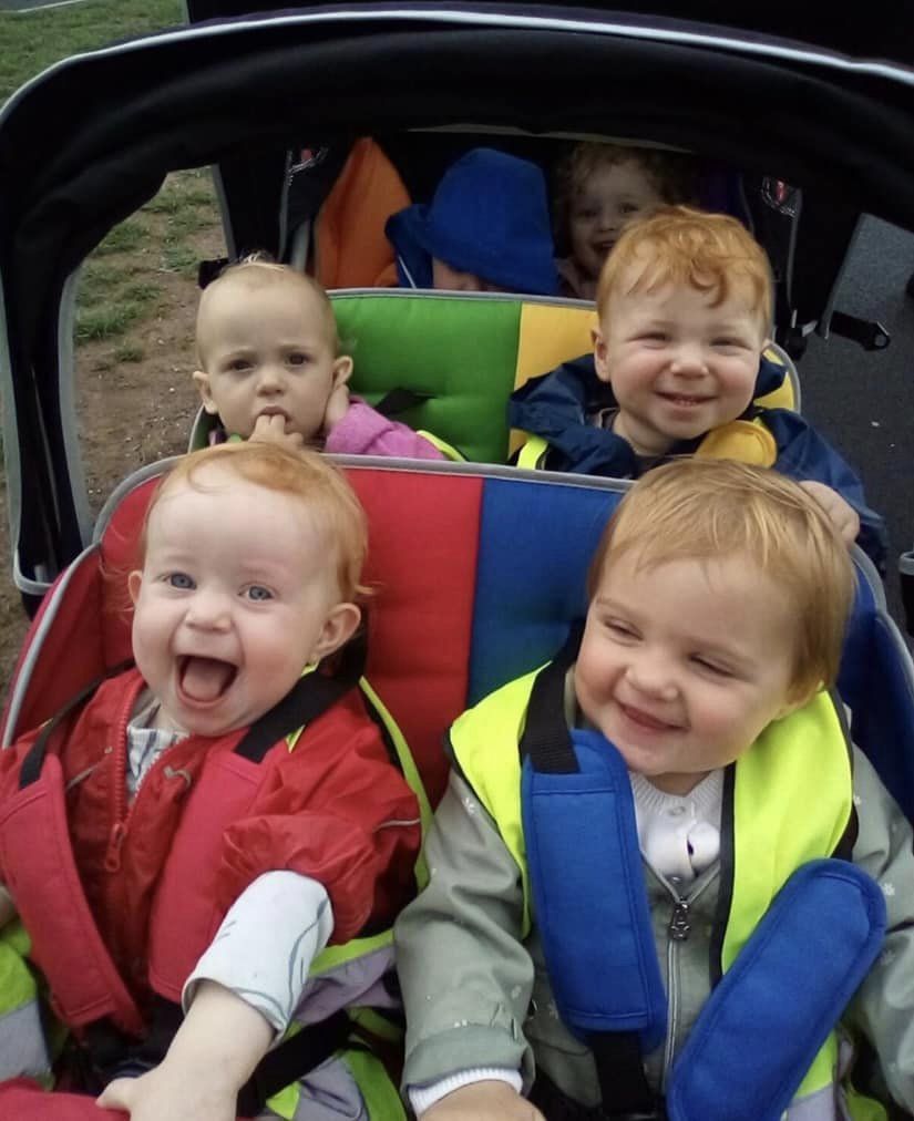 Five toddlers smiling in a colorful stroller.