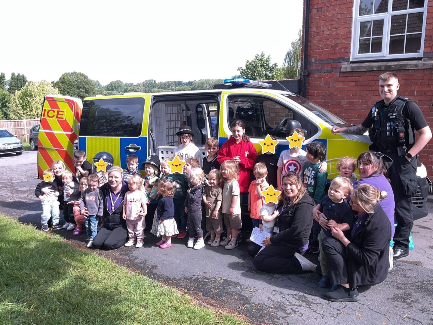 Children and adults pose with a police van on a sunny day.