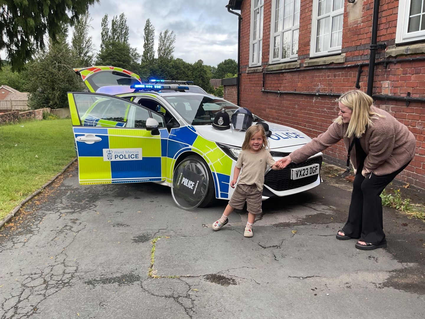 Child and woman near a police car with open door. The car has flashing blue lights.