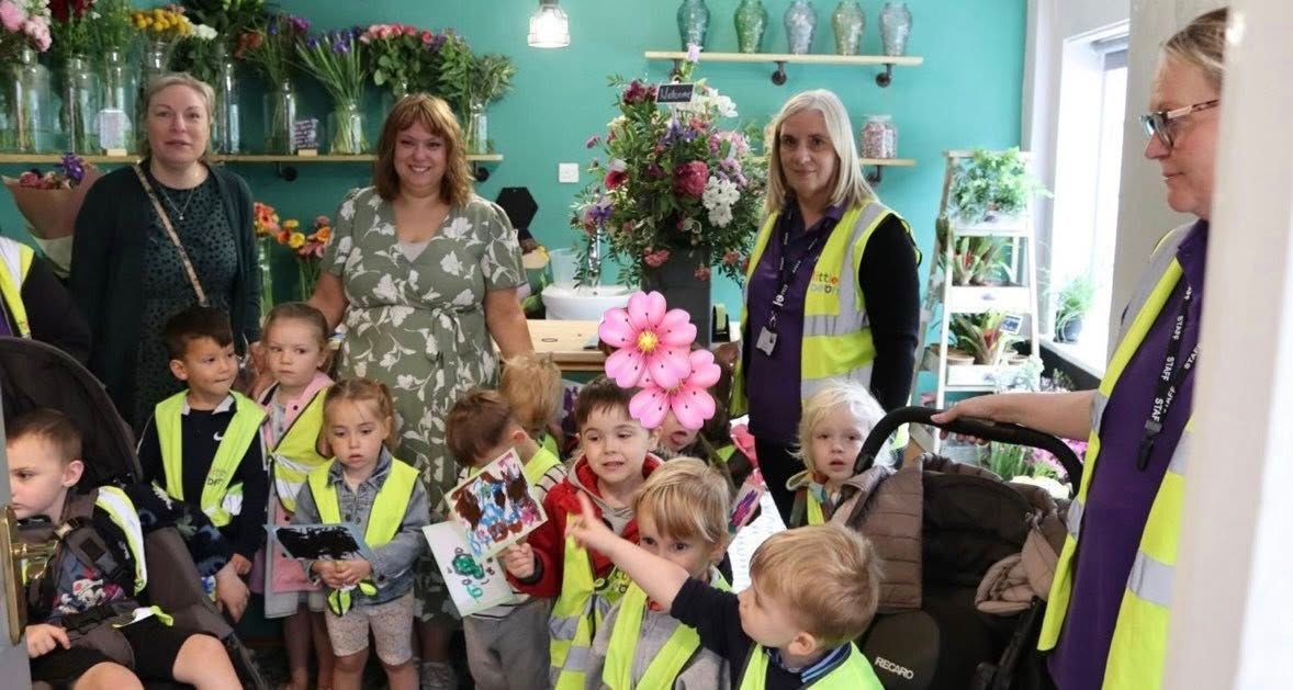 Children and adults in a flower shop. Group of kids wearing vests, looking at flowers. Shop interior with bouquets.