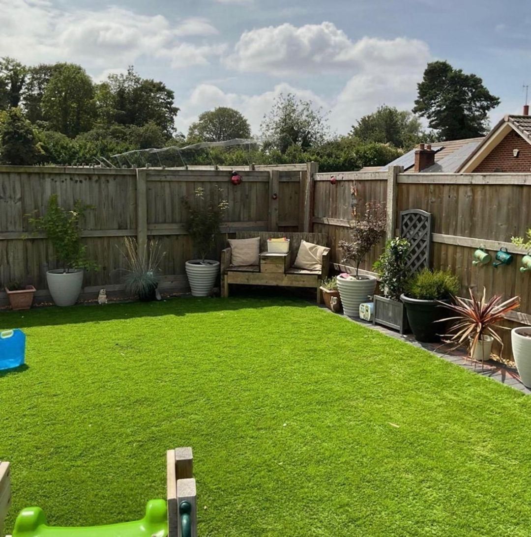 Lush green backyard with a wooden fence, bench, and potted plants. Bright sunny day.