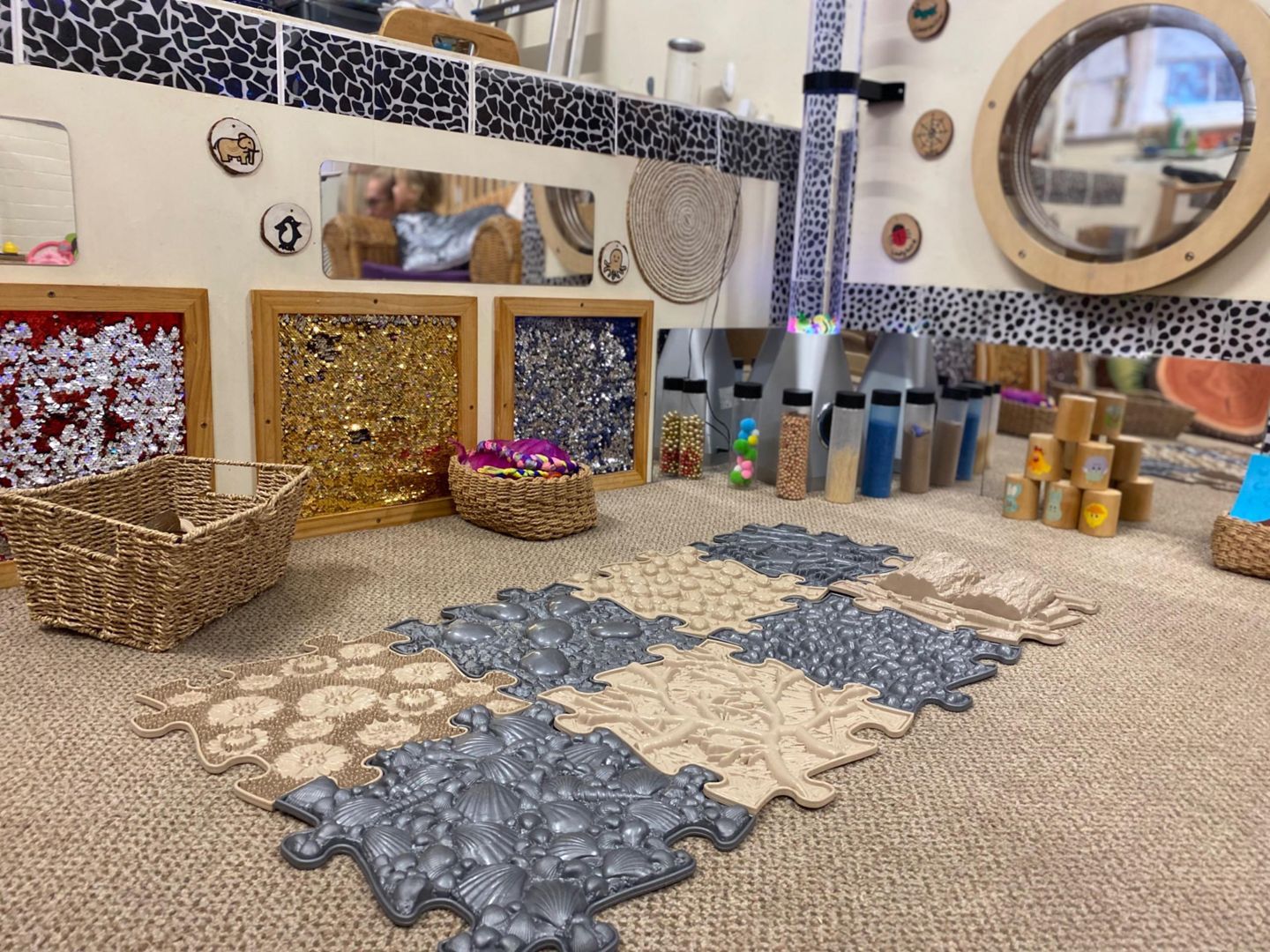 Sensory play area with mirrors, textured tiles, baskets, and containers with colorful materials.