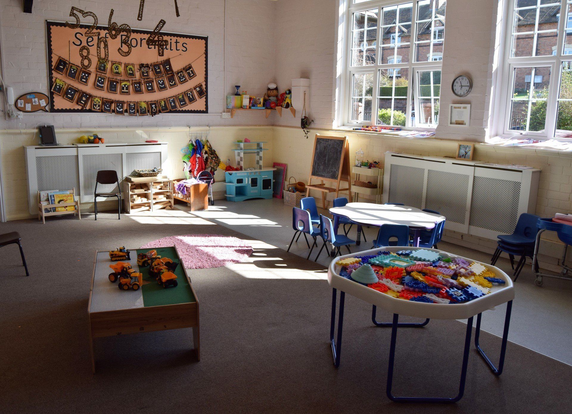 A brightly lit preschool classroom with toys, tables, and a window with sunlight streaming in.