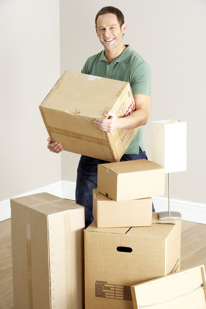 A Man is Holding a Box in Front of a Pile of Cardboard Boxes — Johns Removals Newcastle In Wyong, QLD