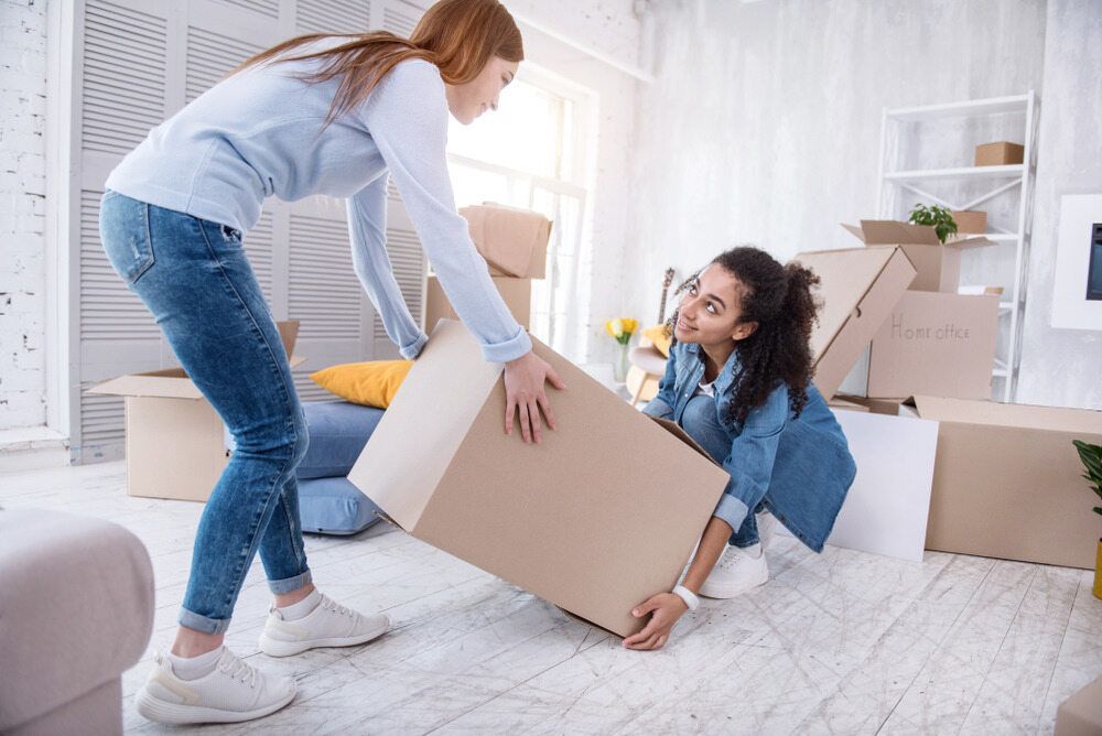 Two Women Are Carrying Boxes in a Living Room — Johns Removals Newcastle In Maitland, NSW