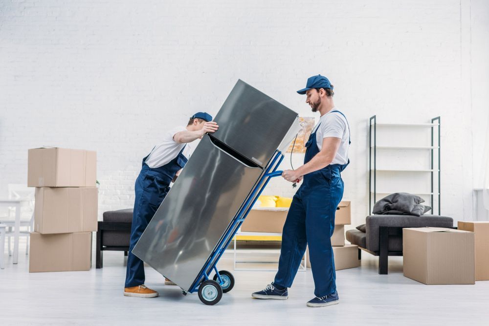 Two Men Are Carrying a Refrigerator on a Dolly in a Living Room — Johns Removals Newcastle In Rankin Park, NSW