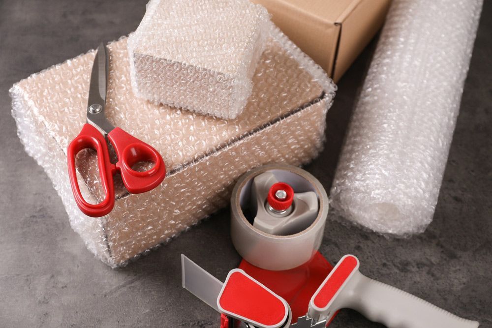 A Pair of Scissors, a Tape Dispenser, and Bubble Wrap Are on a Table — Johns Removals Newcastle In Newcastle, NSW