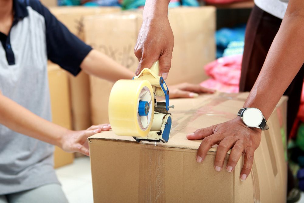 A Man is Using a Tape Dispenser to Tape a Cardboard Box — Johns Removals Newcastle In Rankin Park, NSW