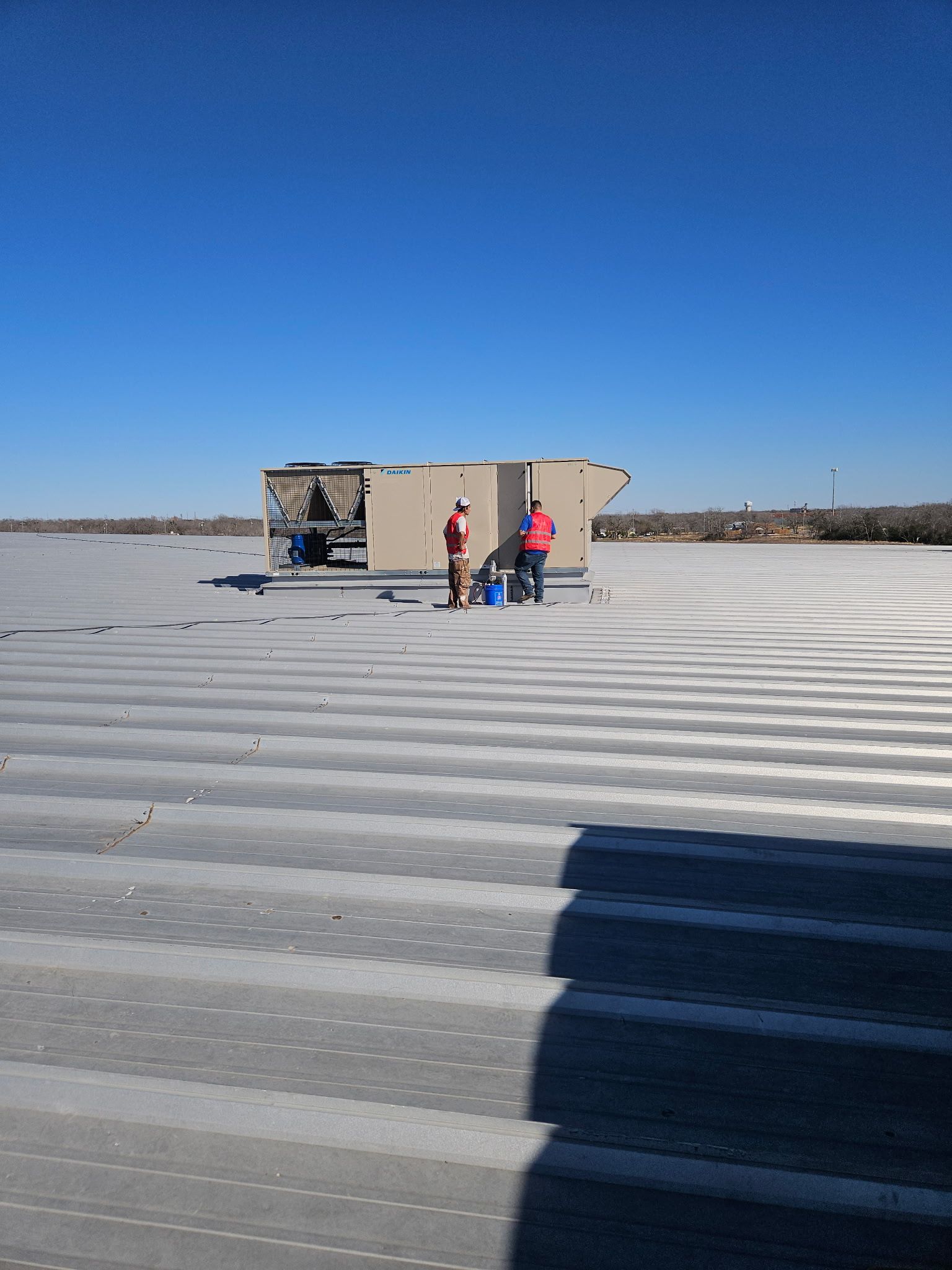 Two people on a flat rooftop with HVAC unit, clear blue sky.