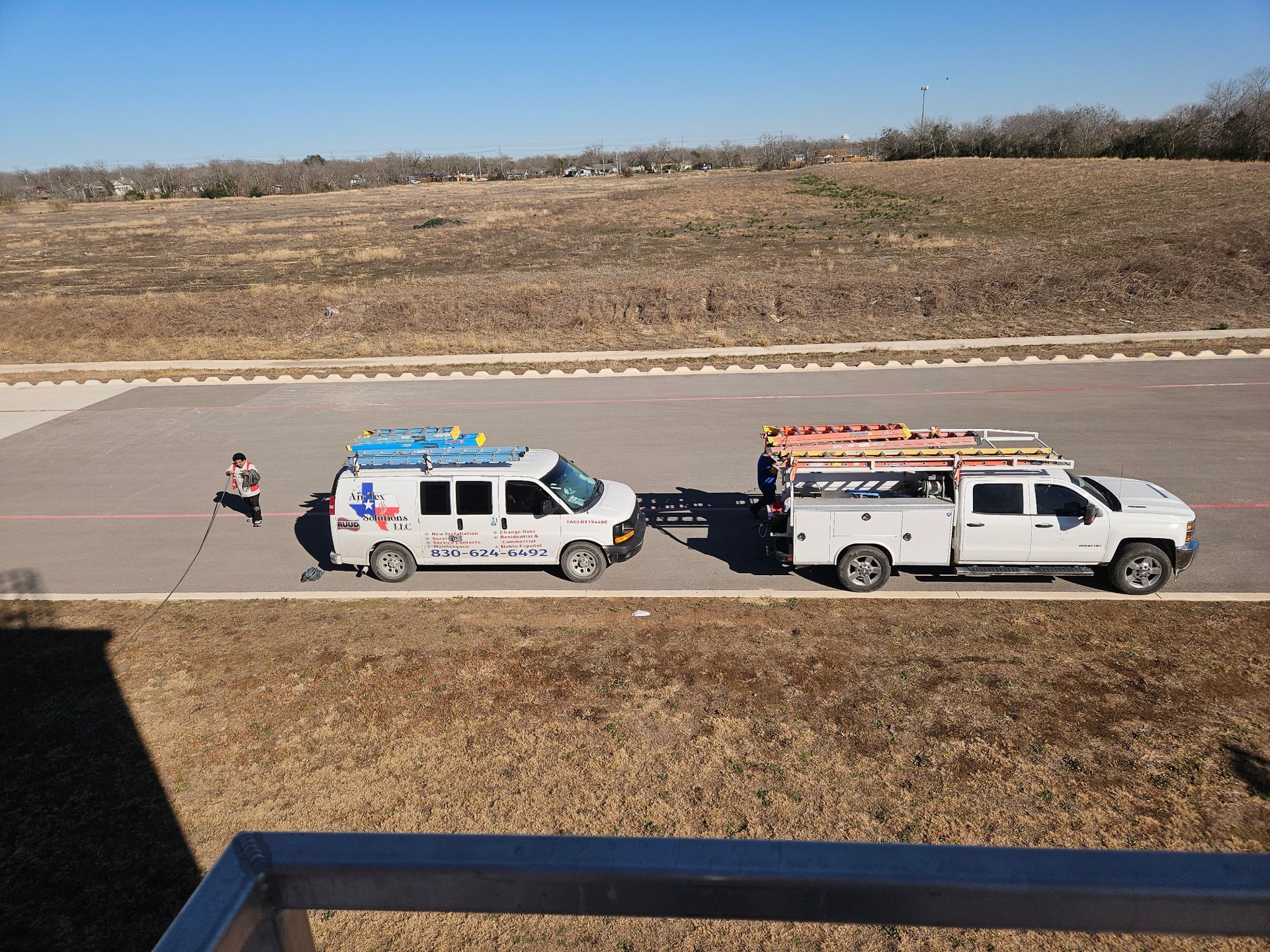 Two work trucks with ladders parked on a paved area, a person standing nearby.