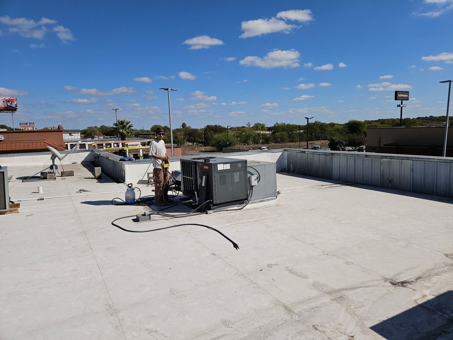 Rooftop with HVAC unit being worked on. Blue sky, white clouds, and city in the background.