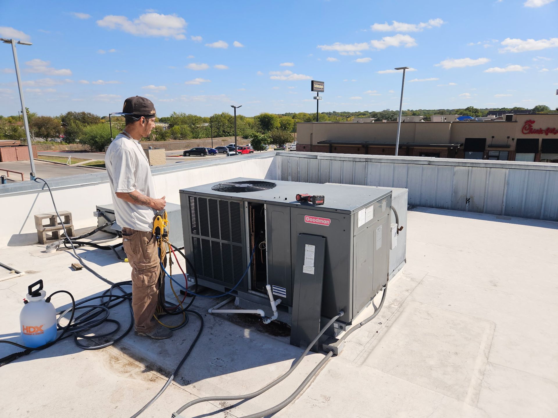 Person working on HVAC unit on rooftop with Chick-fil-A in background. Sunny day.