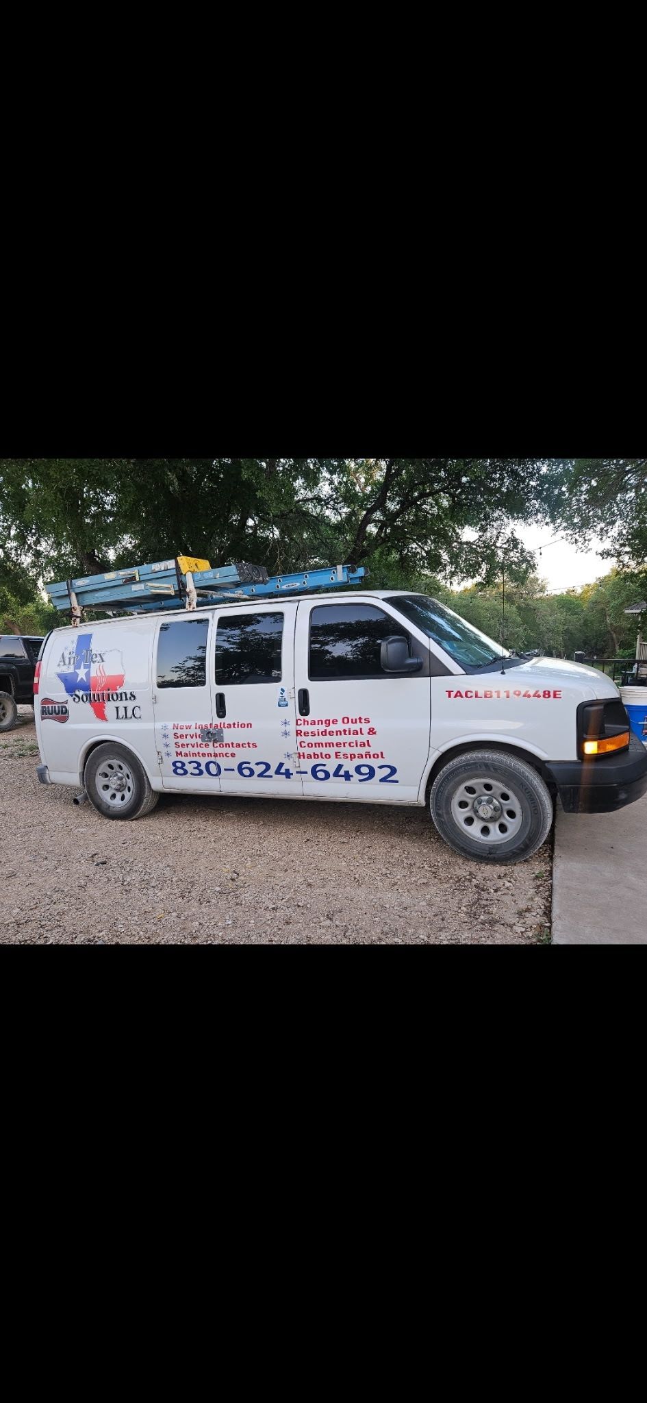 White van with Texas flag logo and phone number, parked on gravel. Blue kayaks on roof rack.