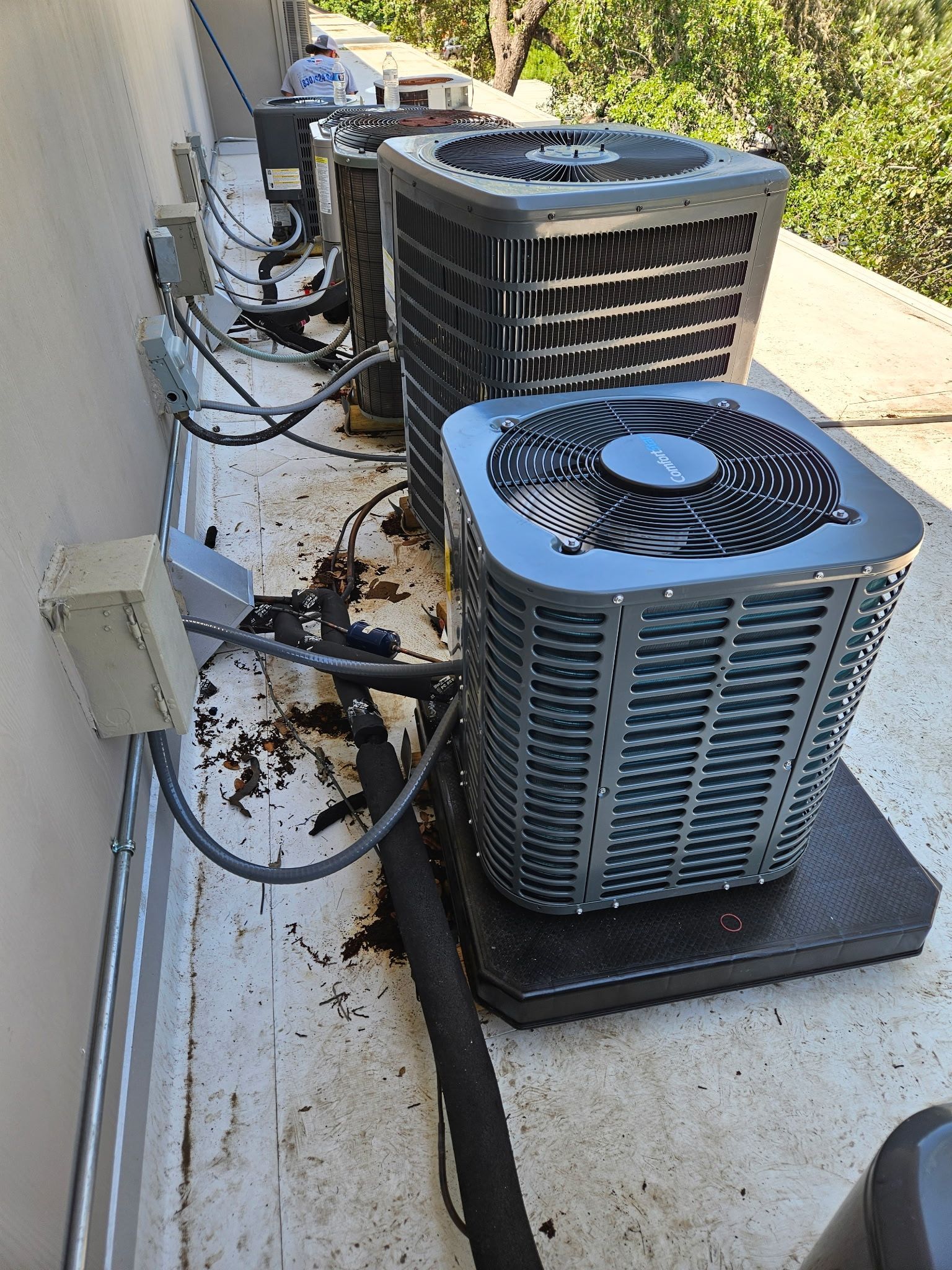 Air conditioning units lined up on a rooftop with electrical connections and debris.